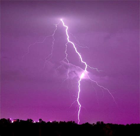 A Purple Sky With Lightning Striking In The Distance And Some Trees On