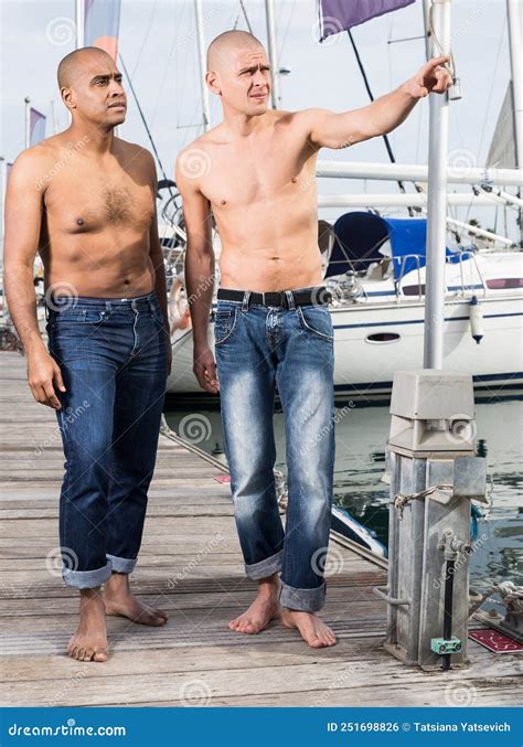 Two Guys Without Shirts In Jeans Walk Barefoot By The Handle Near