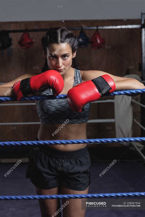 Tired Boxer In Boxing Gloves Leaning On Ropes Of Boxing Ring At Fitness