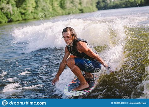 Young Athletic Man With Long Hair Wakesurfing On Waves Of River In