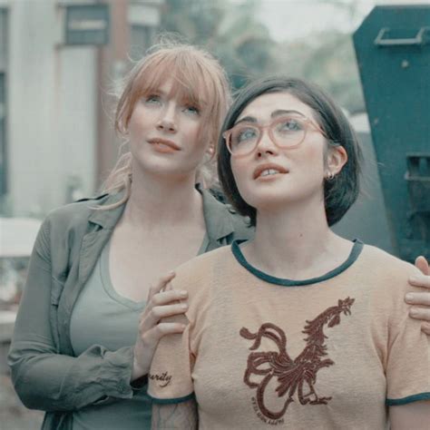 Two Women Standing Next To Each Other In Front Of A Dumpster And Garbage Can