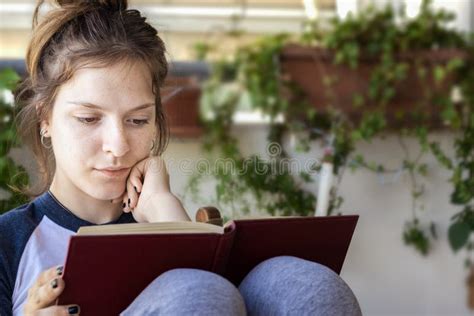 A Young Girl Is Reading A Book Sitting At Home Stock Photo Image Of