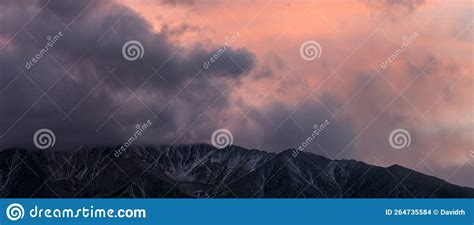 Panorama Of Storm Clouds Hovering Over Snow Capped Mountains At Sunset