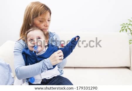 A Mother Dressing Her Serious Boy At Home Stock Photo