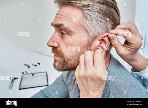 Audiologist Inserting Ite Hearing Aid In Adult Mans Ear At Audiology