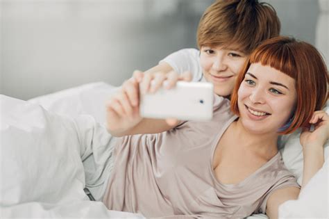 Two Beautiful Lesbians Taking A Selfie While Lying On The Bed Stock