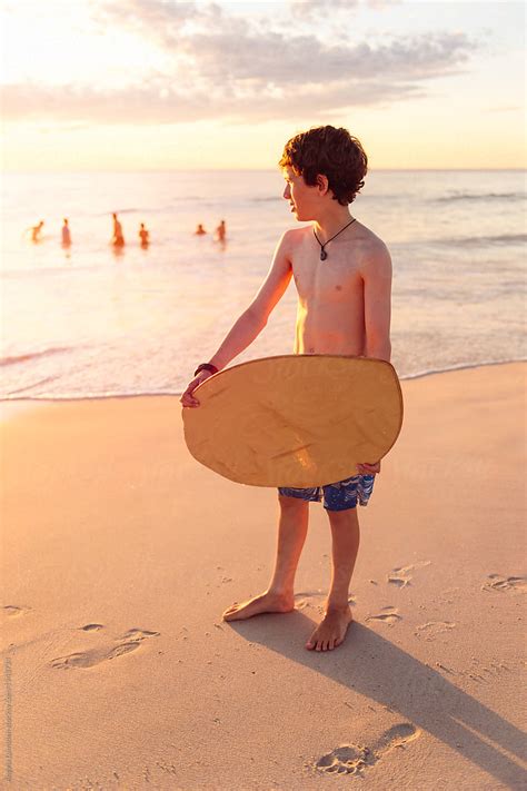 Boy Holding A Skim Board At The Beach At Sunset Del Colaborador De