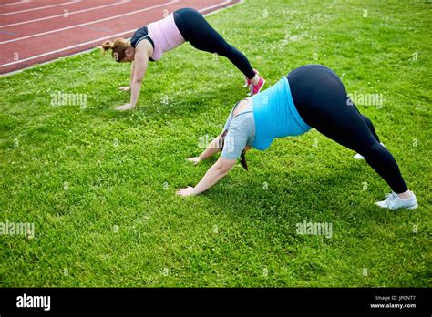 Two Young Active Fat Women Bending Over Lawn With Stretched Arms And