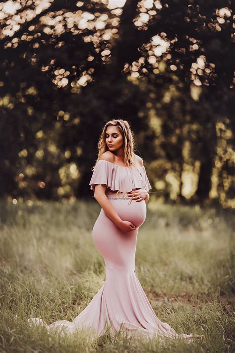 a pregnant woman in a pink gown poses for a photo while standing in tall grass