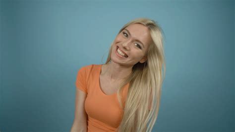 Beautiful Playful Laughing Woman With Long Blonde Hair Posing In Orange T Shirt Against A Blue