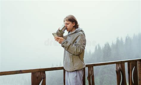 Male Tourist Stands In The Morning On The Terrace Of A Cottage In The