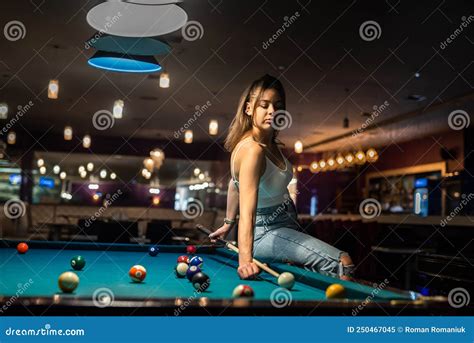 Glamorous Brunette Woman Holding A Cue And Sitting On The Billiard