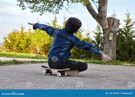Kid Skateboarder Sitting On His Skateboard And Feels Happy Stock Photo