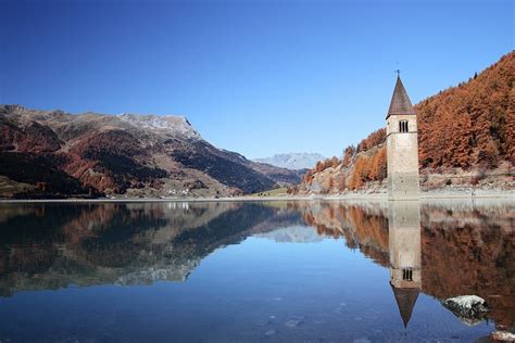 A Clock Tower Sitting In The Middle Of A Lake With Mountains In The