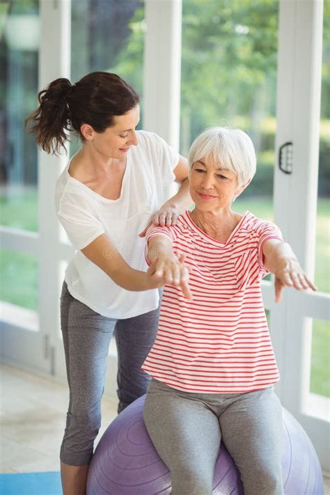 Female Trainer Assisting Senior Couple In Performing Exercise Stock