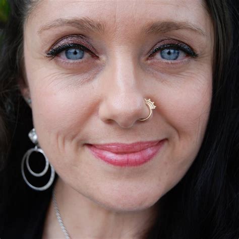 A Close Up Of A Woman With Blue Eyes And Nose Piercings Smiling At The Camera