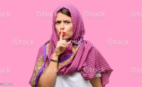 Young Arab Woman Wearing Hijab With Index Finger On Lips Ask To Be