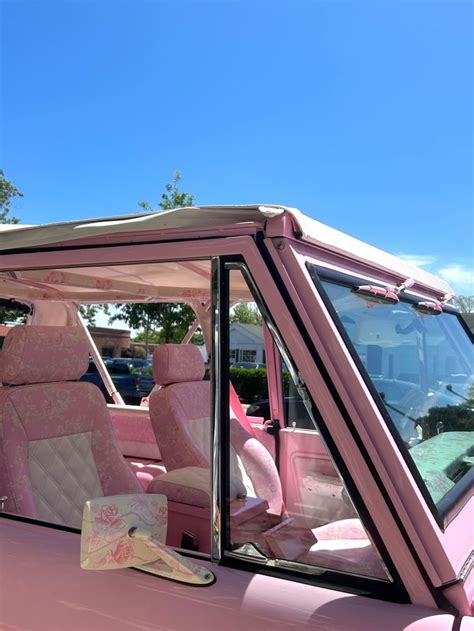 A Pink Car Parked In A Parking Lot With Its Door Open And The Seat Up