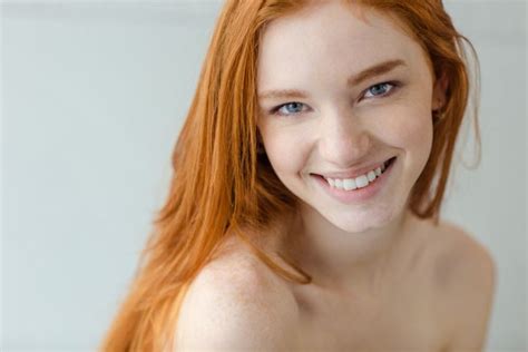 Portrait Of A Smiling Redhead Woman Looking At Camera On Gray