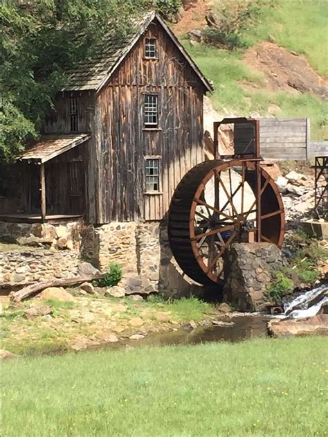 An Old Mill Sits On The Side Of A River Next To A Wooden Building With