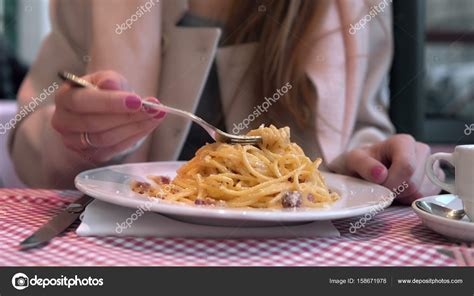 Молодая счастливая женщина сидит за столом в кафе и наслаждается едой