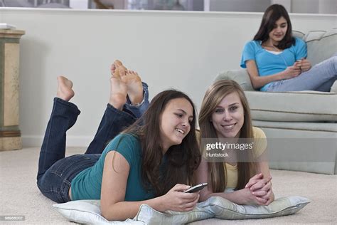 Two Teenage Girls Watching Television With Her Friend Listening To An Mp3 Player High Res Stock