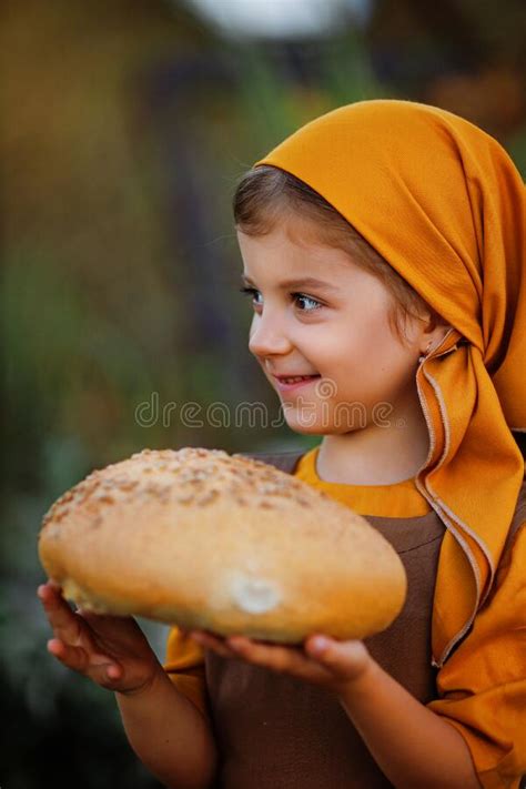 A Small Ukrainian Girl In A Bright Orange Scarf And A Brown Dress Is