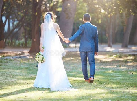 Rear View Shot Of Newlywed Couple Walking Together In Nature Bride And