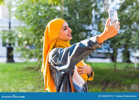 muslim girl in hijab makes a selfie on the phone standing on the street of the city foto de