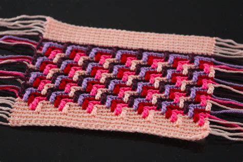 A Close Up Of A Knitted Piece Of Cloth On A Black Surface With Pink
