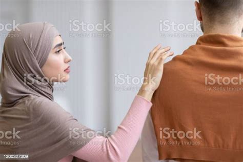 Unhappy Arab Wife In Hijab Touching Husbands Shoulder Standing Indoor