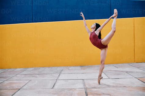 side view of flexible ballerina balancing on leg in split while performing on pavement near