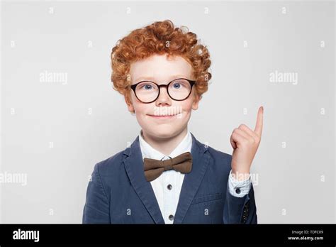 Happy Kid With Ginger Hair Pointing Up And Smiling On White Background