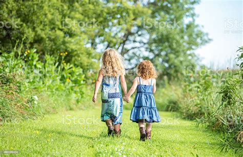Rear View Of Two Young Sisters Walking Holding Hands Stock Photo