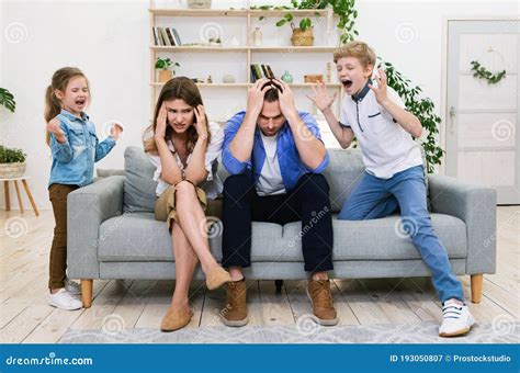 Naughty Kids Shouting Loudly Standing Near Tired Parents At Home Stock