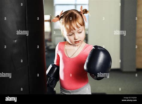 Little Girl In Big Boxing Gloves Fight With Pear In The Gym Stock Photo