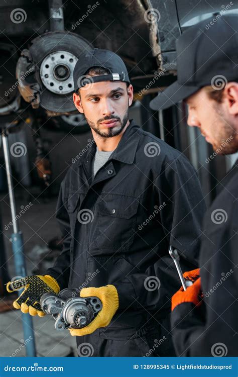 Professional Car Mechanics Working Under Lifted Car In Auto Repair