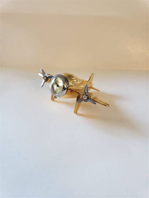 A Gold And Silver Airplane Brooch Sitting On Top Of A White Surface