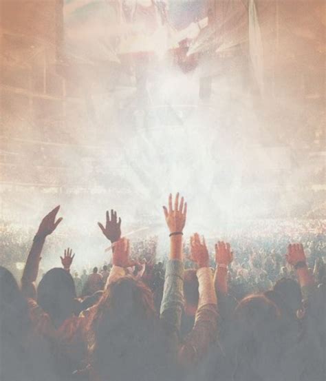 A Crowd Of People At A Concert With Their Hands In The Air And Lights