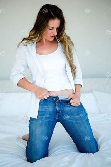 Woman Kneeling On Her Bed Struggling To Button Her Jeans Stock Image Image Of Attentively