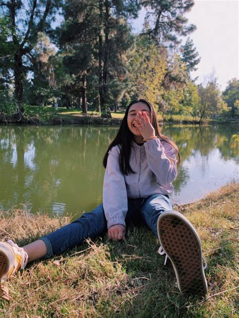 A Woman Sitting On The Ground Next To A Lake With Her Hand In Her Face