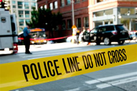 Focus On Police Yellow Crime Scene Tape With Scene In Rear Stock Photo