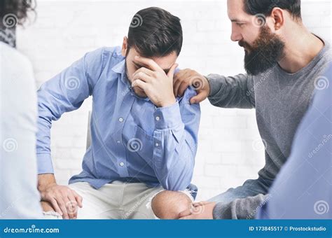 Concerned Patients Comforting Upset Man At Group Therapy Session In
