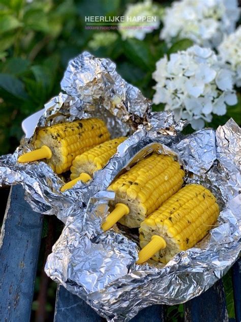 Grilled corn on the cob in aluminum foil with white flowers behind it