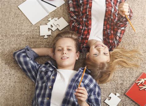 Brother And Sister Doing Homework Lying On Floor At Home Stock Photo