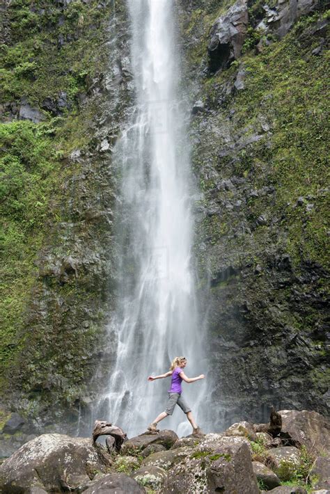Hiker Leaping In Front Of A Waterfall Along The Famous Kalalau Trail