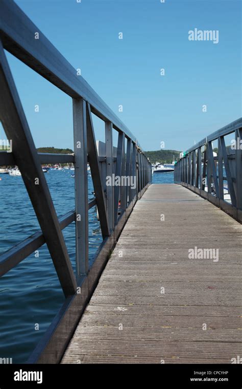 A Seaside Pier With Metal Railings And Boats In The Background Stock