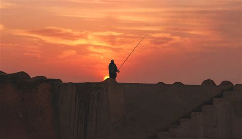 A Silhouette Of A Fisherman Standing Atop A Wall In Asilah Morocco