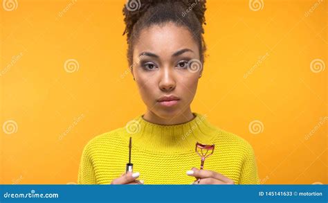 Young Afro American Female Holding Mascara Brush And Eyelash Curler