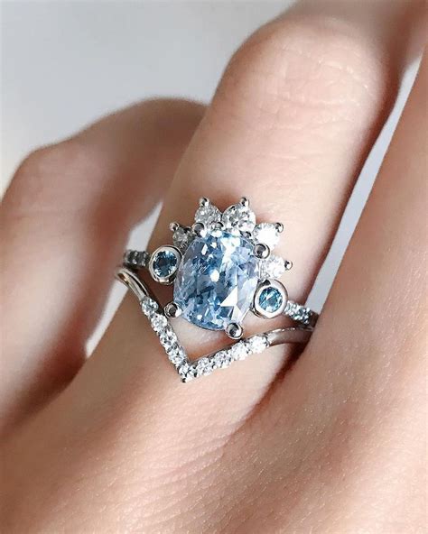 a woman s engagement ring with an oval blue diamond surrounded by white topaz